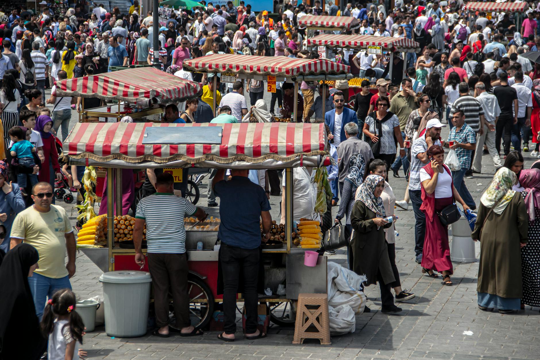 Multitud de personas rodeando varios carritos de comida tradicional en una plaza turca.