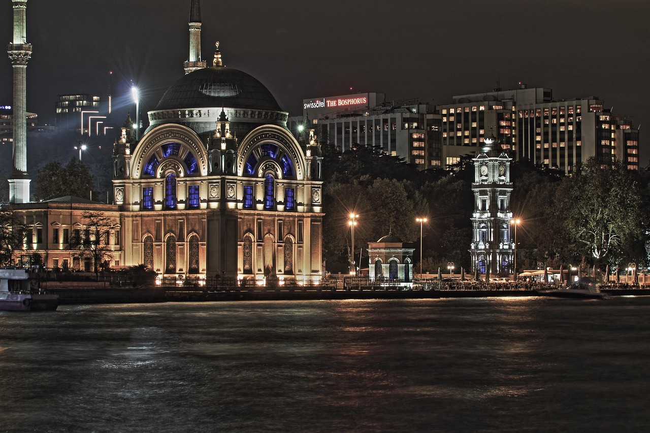 Mezquita de Dolmabahçe y torre del reloj iluminadas junto al Bósforo de noche.