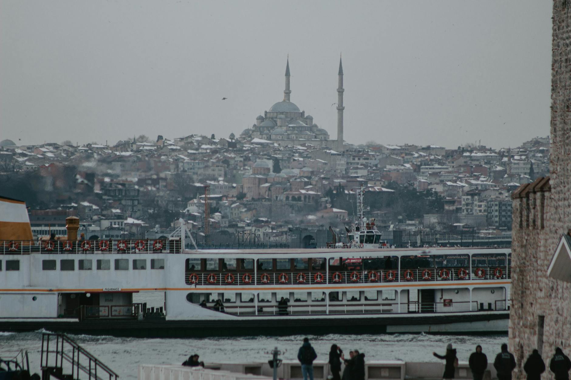 Un barco de pasajeros cruza las aguas del Bósforo con mezquitas nevadas al fondo.