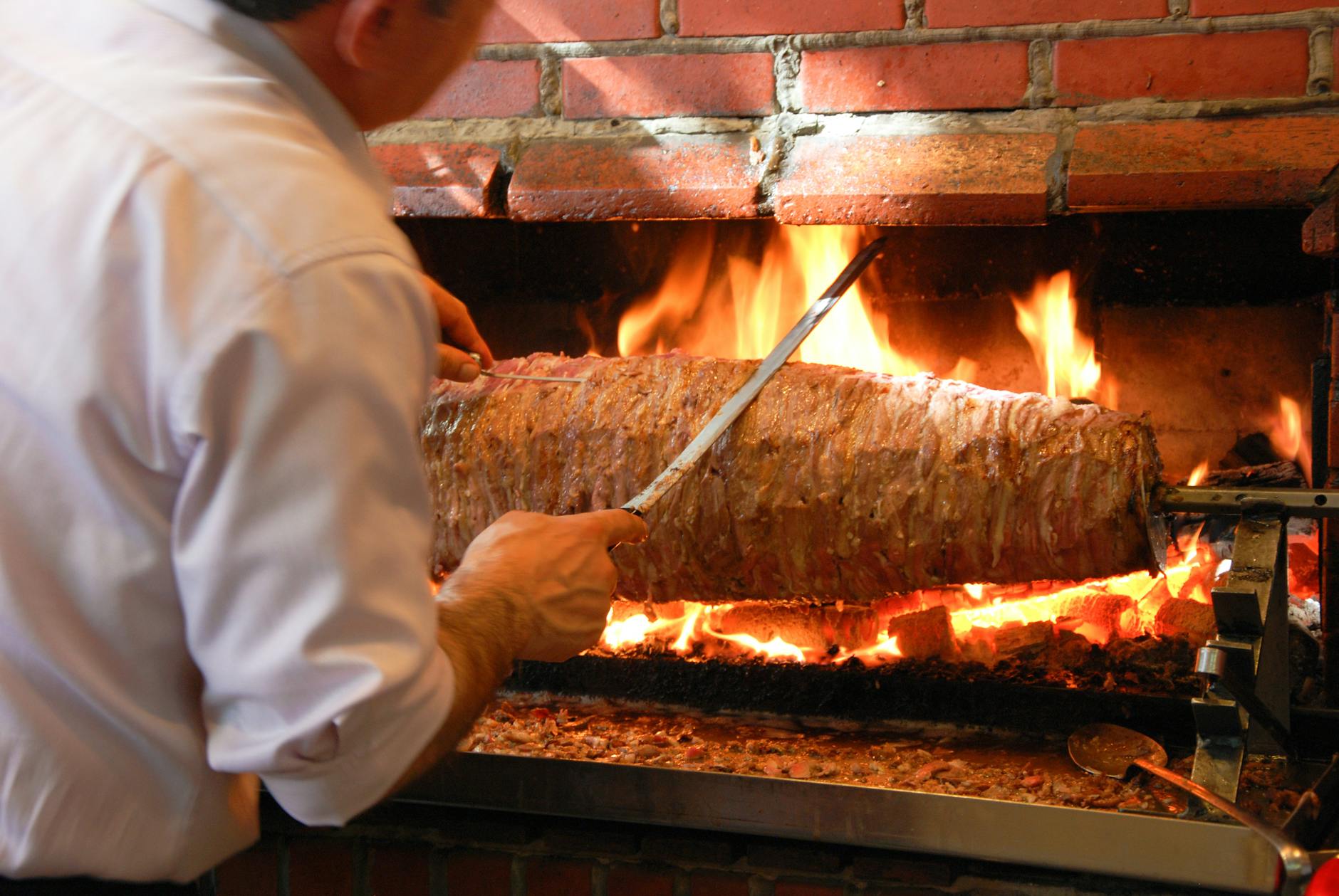 Maestro parrillero cortando cordero de Erzurum cocinado en un asador horizontal tradicional.