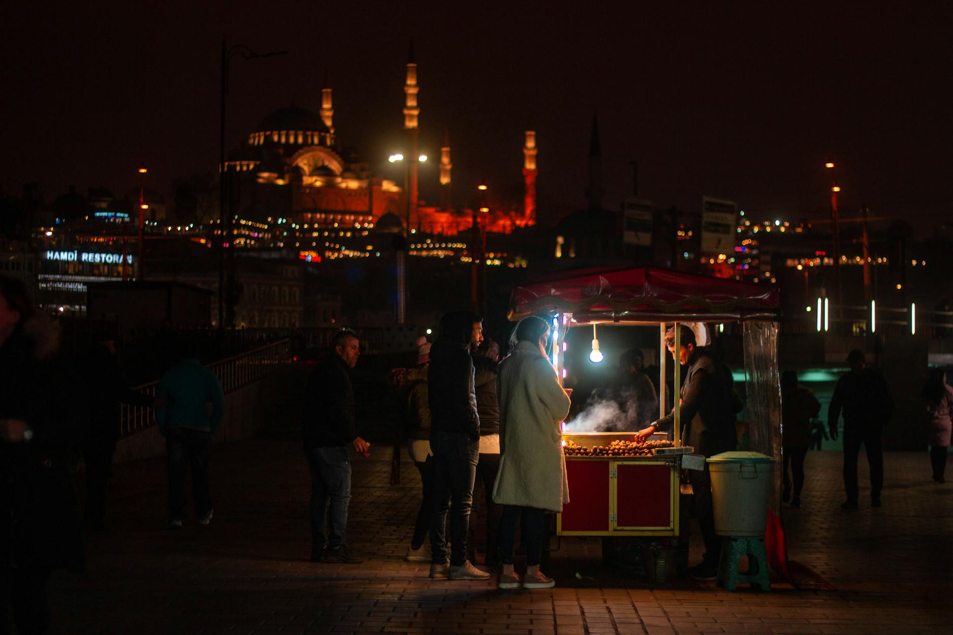 Puesto callejero de castañas asadas con una mezquita iluminada al fondo en Estambul.