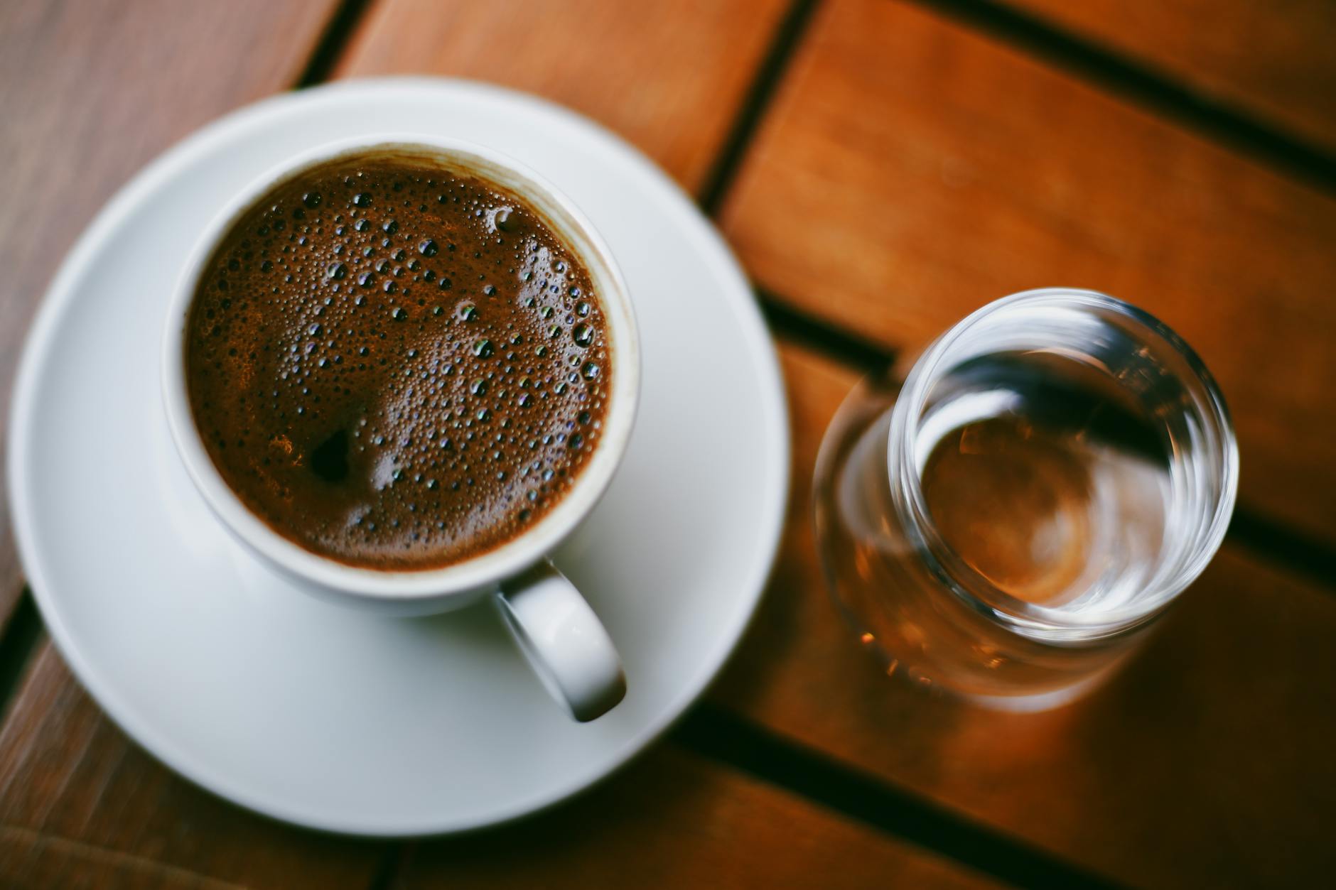 Primer plano de un café tradicional espumoso acompañado por un pequeño vaso de agua.