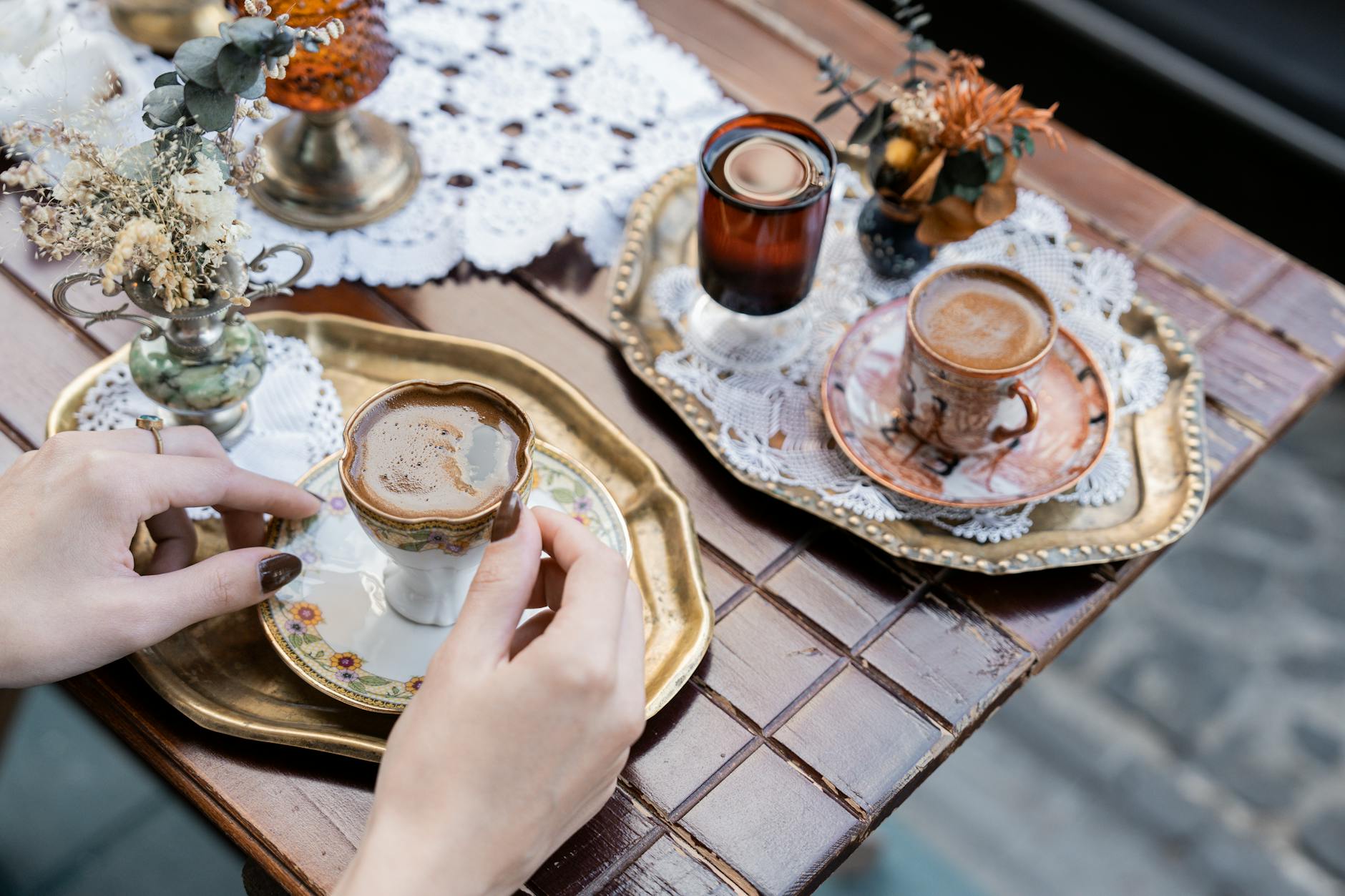 Manos sosteniendo una pequeña taza de café servida sobre una bandeja dorada decorada.